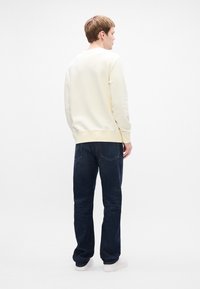 Jasnożółty sweatshirt z okrągłym dekoltem, w zestawieniu z ciemnoniebieskimi dżinsami. Prosty design, gładka tekstura i prosty krój. Białe sneakersy.
