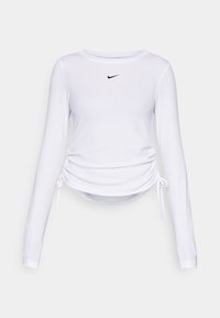 Haut à manches longues blanc avec un col rond, présentant un logo Nike noir au centre et un ruché sur les côtés ajustable avec des liens. Matériau doux.