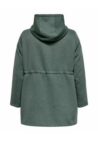 Kapuca z oversized plaščem v temno zeleni barvi, izdelan iz mehkega, teksturiranega blaga. Ima zategnjen pas in preprost, minimalističen dizajn.