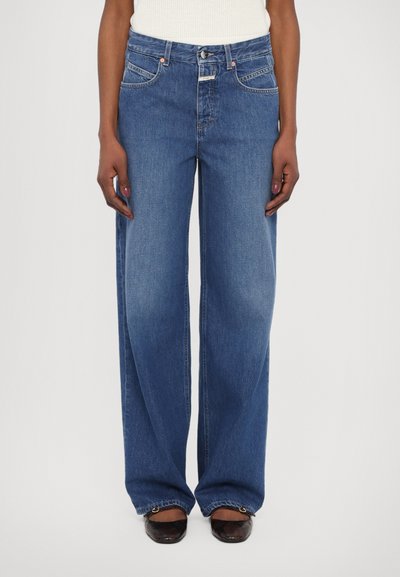 Jeans w szerokich nogawkach w średnim odcieniu niebieskiego. Posiada pięć kieszeni, zapięcie na guzik i zamek błyskawiczny oraz kontrastowe szwy. Tekstura jest gładka.