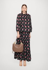 Svart blomstret kjole med lange puff-sleeves, parret med en brun buet håndveske. Mykt stoff med mønstre av rosa og grønne blomster.