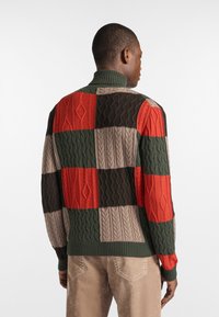 Strickpullover in Grün, Rot, Braun und Beige. Besticht durch ein Patchwork-Design mit strukturierten Zopfmustern. Hoher Kragen und gerippte Bündchen.