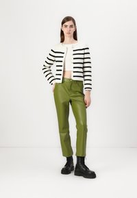 Svart og hvit stripete cardigan med gullknapper, kombinert med skinnende grønne imitert lærbukser og svarte snørestøvler.