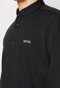 Schwarzes Hemd mit Knopfleiste, schmalem Schnitt, Kragen und dem Markennamen "BOSS" dezent in Hellgrau auf der Brust bestickt.