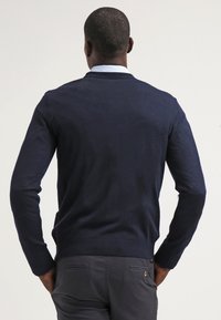 Mörkblå, stickad tröja med rund halsringning och långa ärmar. Slät textur, figurnära design, bakvy med ribbad fåll och muddar.