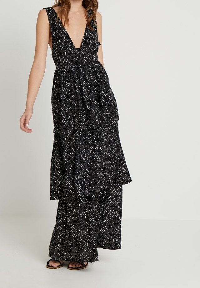 Abito nero a strati con scollatura a V profonda e maniche a volant, caratterizzato da un motivo a pois bianchi sparsi. Tessuto leggero, design fluido.