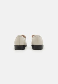 Lichtbeige leren schoenen met een strakke vormgeving, ronde hakken en contrasterende zwarte zolen. Beschikken over minimale stiksels en een gladde textuur.