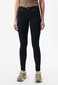 Pantalones cargo negros ajustados con bolsillos laterales, confeccionados en un material de mezclilla elástica, con una cintura alta y una textura suave.