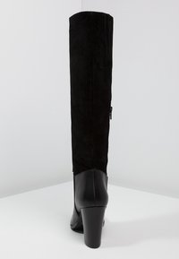Bota negra hasta la rodilla con parte superior de ante y tacón de cuero. Presenta un diseño elegante, forma sólida y cremallera lateral para facilitar el uso.