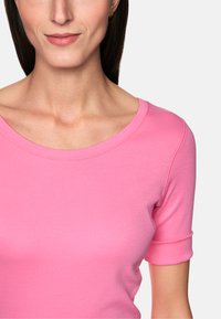 Short-sleeve top in bright pink fabric, featuring a ribbed texture and a round neckline with a subtle seam detailing around the edges.