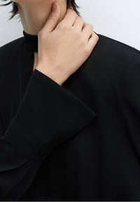 Haut en tissu noir avec un design à col montant et de larges manches structurées. La texture semble lisse avec des coutures minimalistes et un détail de bouton unique.