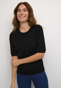Fekete, rövid ujjú, kerek nyakú kötött felső, sima textúrával és szűkített fazonnal, kék farmernadrággal párosítva.