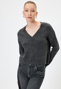 Pull en tricot gris à côtes avec un col en V et des manches longues, fabriqué en matériau doux. Associé à un jean denim foncé. Design simple et ajusté.