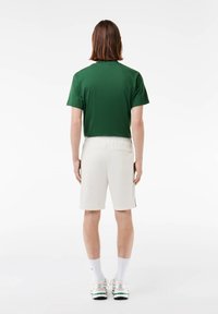 T-shirt vert à manches courtes avec un col rond, associé à un short blanc jusqu'aux genoux. Le short dispose d'une taille élastique texturée.