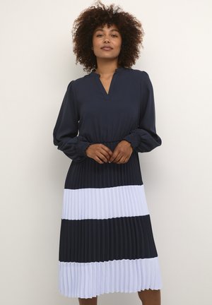 Navy blue dress with long sleeves, pleated lower section featuring alternating navy and white stripes, and a V-neckline.