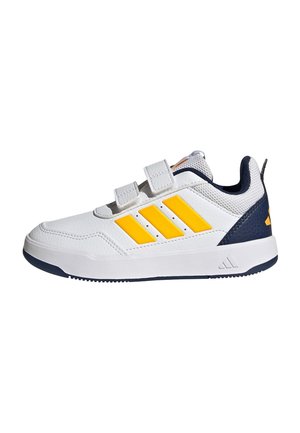 Zapatilla blanca con rayas amarillas, talón azul marino y dos tiras de velcro sobre un fondo blanco.