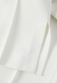 Gros plan sur un tissu blanc avec une couture ajustée et une fente latérale, mettant en valeur la texture et la construction du vêtement.