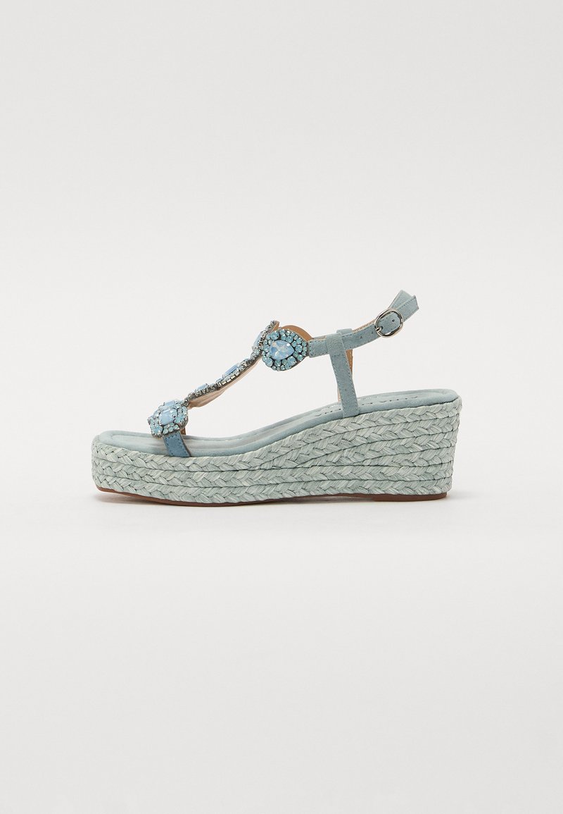 Sandale compensée bleu clair avec semelle en jute tressé, ornée de pierres décoratives sur la bride et d'une boucle ajustable à la cheville.