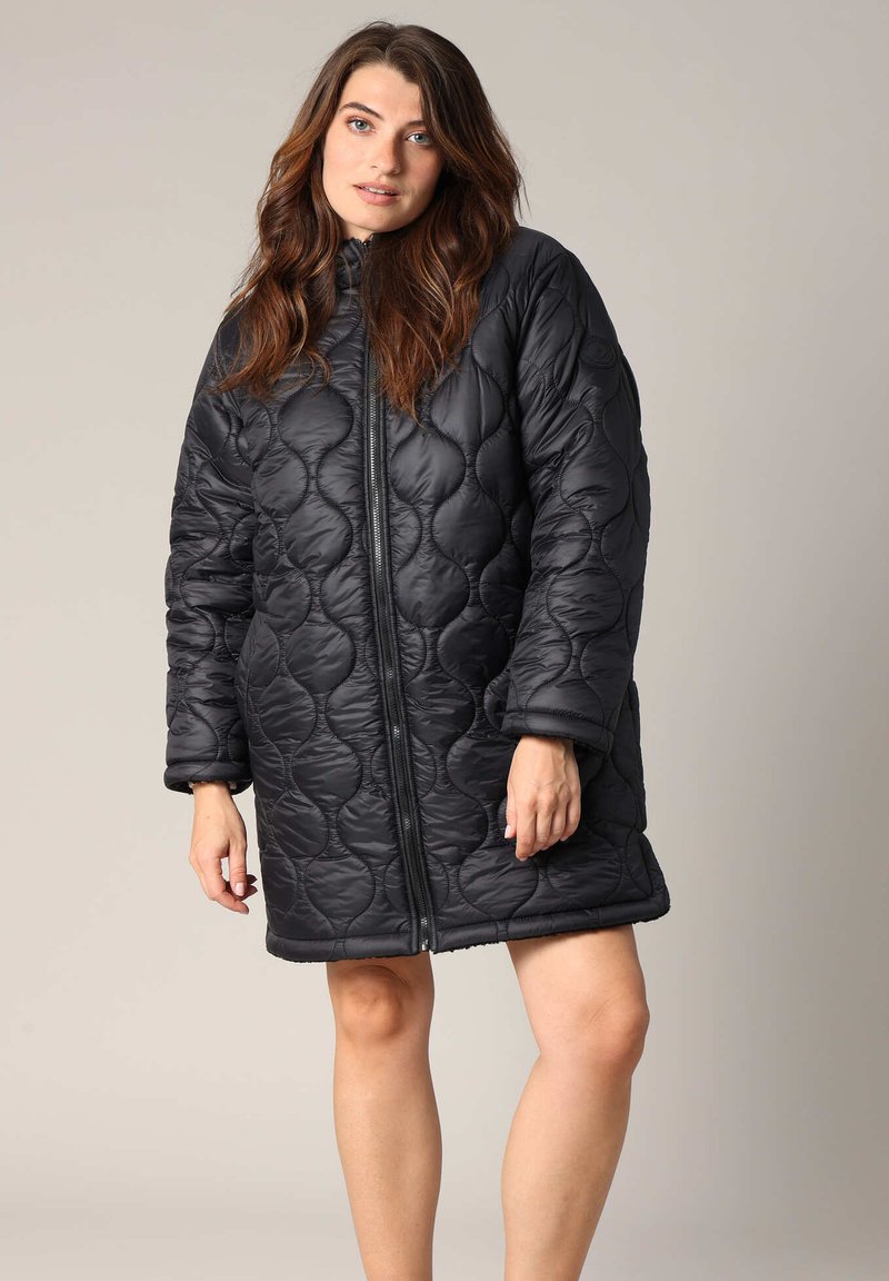 Manteau matelassé noir avec fermeture éclair, encolure arrondie et coupe ample. Présente des coutures en motif circulaire et des manches larges.