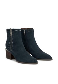 Botas de tobillo de ante azul marino con punta afilada, cremallera lateral y remaches metálicos a lo largo de la costura. Con un tacón de madera apilada.