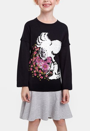 Kind draagt een zwarte top met lange mouwen met een witte hond en roze bloemdessin, gecombineerd met een lichtgrijze rok.