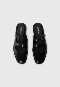 Black, glossy block-heeled mules with open toes. Features two crossed straps and a side buckle. Smooth texture with a square toe design.