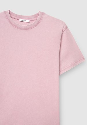T-shirt di cotone rosa chiaro con collo rotondo, maniche corte e dettagli di cucitura sul colletto e sull'orlo. L'etichetta è visibile sul collo.