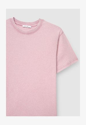 T-shirt di cotone rosa chiaro con collo rotondo, maniche corte e dettagli di cucitura sul colletto e sull'orlo. L'etichetta è visibile sul collo.