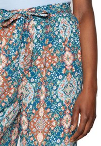 Pantalons à motifs bleus avec des dessins floraux rouges, verts et pêches, dotés d'une taille nouée et d'une coupe décontractée. Tissu en coton doux.