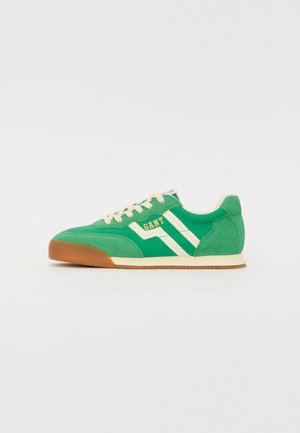 Sneaker verde in camoscio con accenti bianchi e arancioni, un profilo testurizzato e suola in gomma. Le stringhe predominano nella parte superiore.