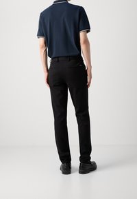 Granatowa koszulka polo z białym obszyciem, zestawiona z czarnymi spodniami, charakteryzująca się eleganckim designem i minimalistycznym detalem tylnej kieszeni. Czarna para butów dopełnia strój.