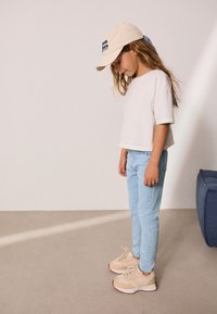 Ljusbeigefärgad bomullströja, ljusblå denimjeans och beiga sneakers med texturerade detaljer. Keps i krämfärg med blå text.