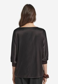 Svart satinblus med avslappnad passform, trekvartslånga ärmar och vid halsringning. Slät textur utan synliga mönster eller detaljer.
