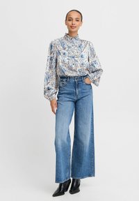 Camicia a maniche lunghe con motivo paisley blu e beige, con colletto arricciato, abbinata a jeans a gamba larga a vita alta in denim blu chiaro.