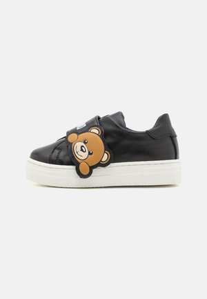 Sneaker in pelle nera con suola in gomma bianca, caratterizzata da un'applicazione a forma di testa d'orso sulla fascia. Il design è a bassa altezza con una finitura testurizzata.
