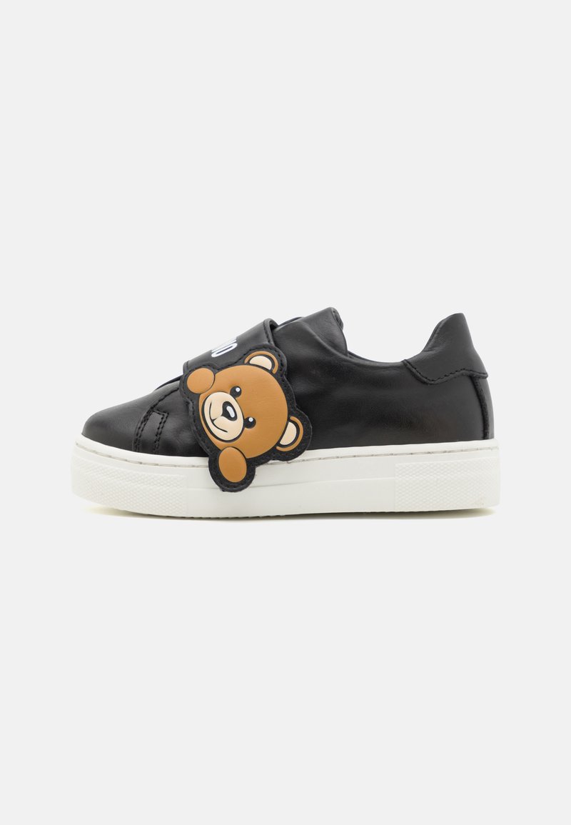 Sneaker in pelle nera con suola in gomma bianca, caratterizzata da un'applicazione a forma di testa d'orso sulla fascia. Il design è a bassa altezza con una finitura testurizzata.