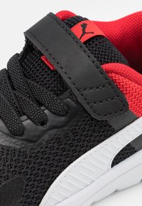 Baskets de sport noires avec une tige en mesh, des accents rouges, une sangle Velcro et une semelle en caoutchouc blanc. Design léger texturé pour une meilleure respirabilité.