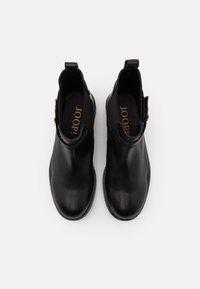 Bottes chevilles en cuir noir avec bout arrondi, panneaux latéraux élastiques et un petit accent décoratif en métal. Texture lisse.