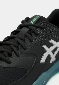 Zapatilla deportiva negra con parte superior sintética texturizada, detalles de malla, logotipo gris, cordones negros y suela de goma color verde azulado. Presenta un diseño aerodinámico.