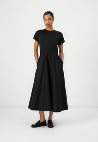 Schwarzes Kleid mit kurzen Ärmeln, tailliertem Oberteil und schwingendem Rock. Aus weichem Stoff gefertigt, mit seitlichen Taschen und knielangem Design.