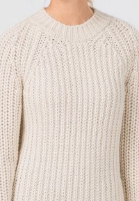 Krämfärgad stickad tröja med ribbat mönster, featuring rund halsringning och raglanärmar för en avslappnad passform. Inga anmärkningsvärda mönster eller accenter.