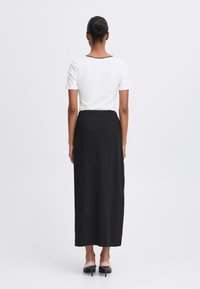Vit kortärmad topp med svart kant, som matchas med en lång svart kjol. Outfiten har en ren, enkel design och en flödande silhuett.