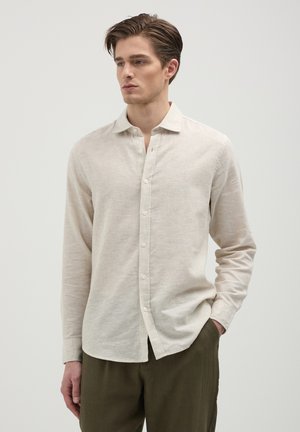 Beige linen long-sleeve shirt with a classic collar and button front. Features a slightly textured fabric and slim fit design, paired with olive-green pants.