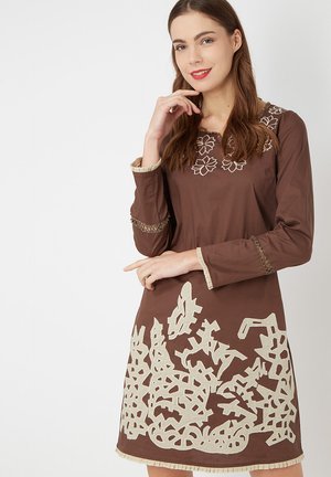 Vestido marrón de mangas largas, con bordados florales blancos en el escote y un intrincado patrón beige a lo largo del dobladillo y las mangas.