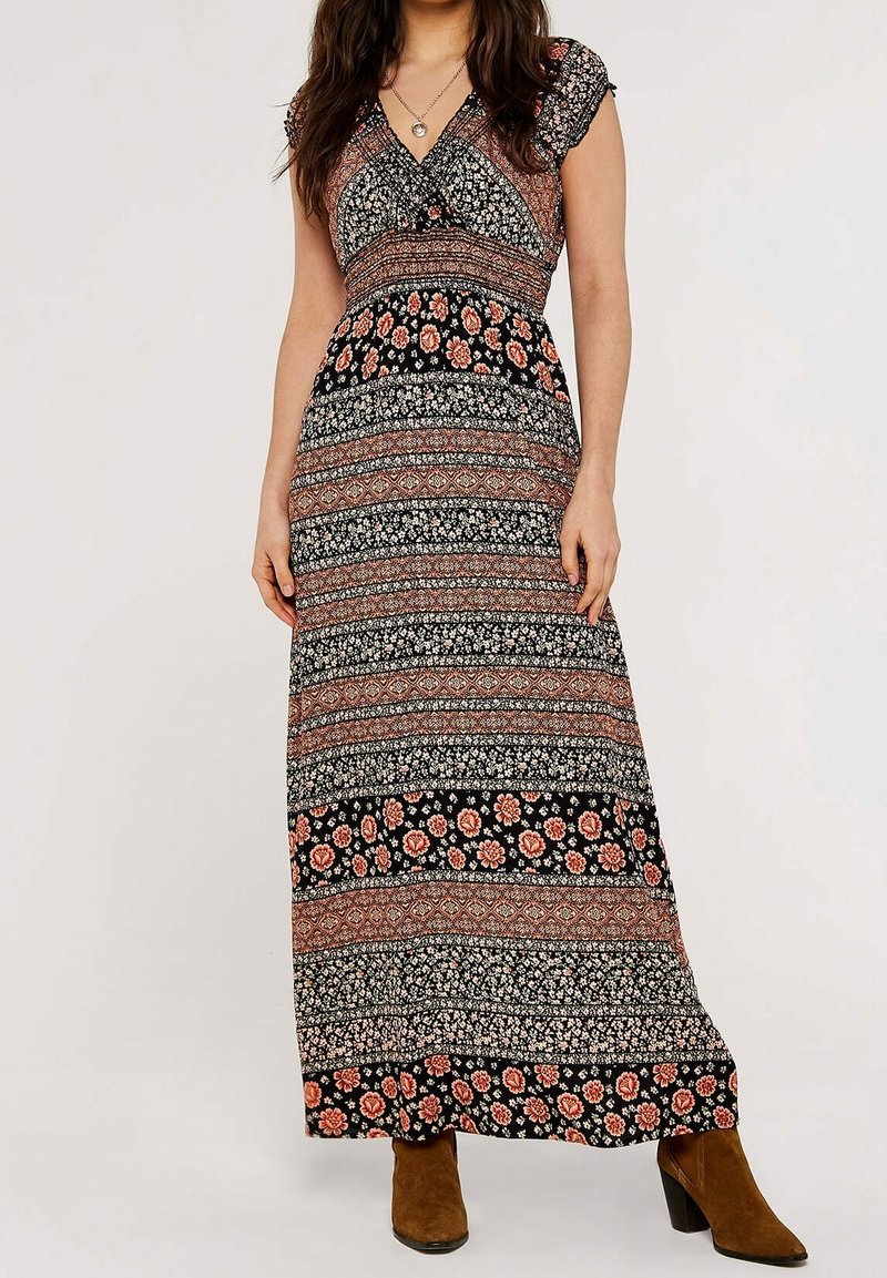 Femme portant une robe longue noire et rouille à motifs floraux et géométriques, avec des manches courtes et des bottines en daim marron.