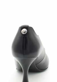 Chaussure à talon haut en cuir noir avec un bout arrondi, un talon fin et un bouton décoratif en argent à l'arrière avec des détails cousus.