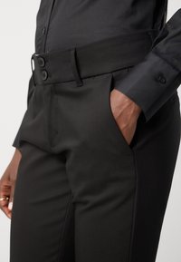 Svarta skräddarsydda byxor med en mjuk struktur, med platt front, bälteshällor och två knappar vid midjan. Innehåller sidofickor.