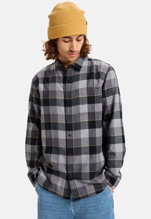 Gray plaid shirt with black and light gray squares, yellow accents, button-up design, and a chest pocket. Model wears a mustard knit beanie.