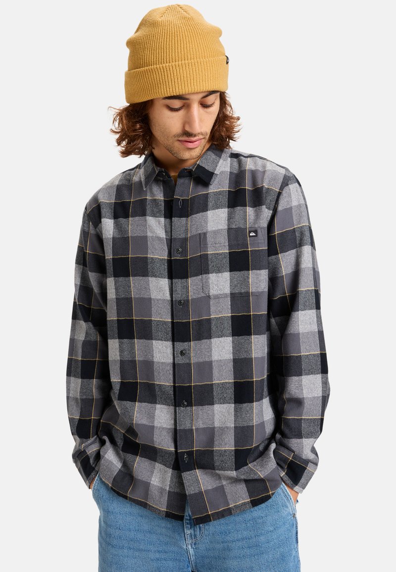Gray plaid shirt with black and light gray squares, yellow accents, button-up design, and a chest pocket. Model wears a mustard knit beanie.