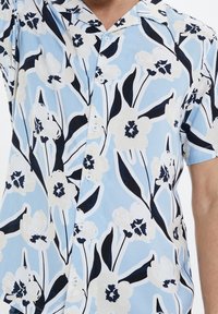 Kurzärmliges Blumenhemd in hellblau, mit großen weißen Blumen und schwarzen Akzenten, einer Knopfleiste vorne und einem klassischen Kragendesign.